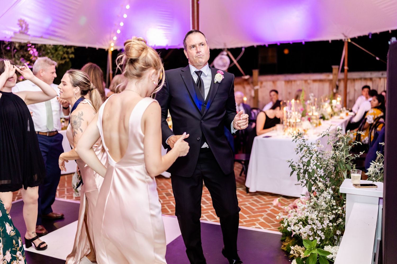Wedding guests dancing and celebrating on a purple-lit dance floor under an elegant tent.