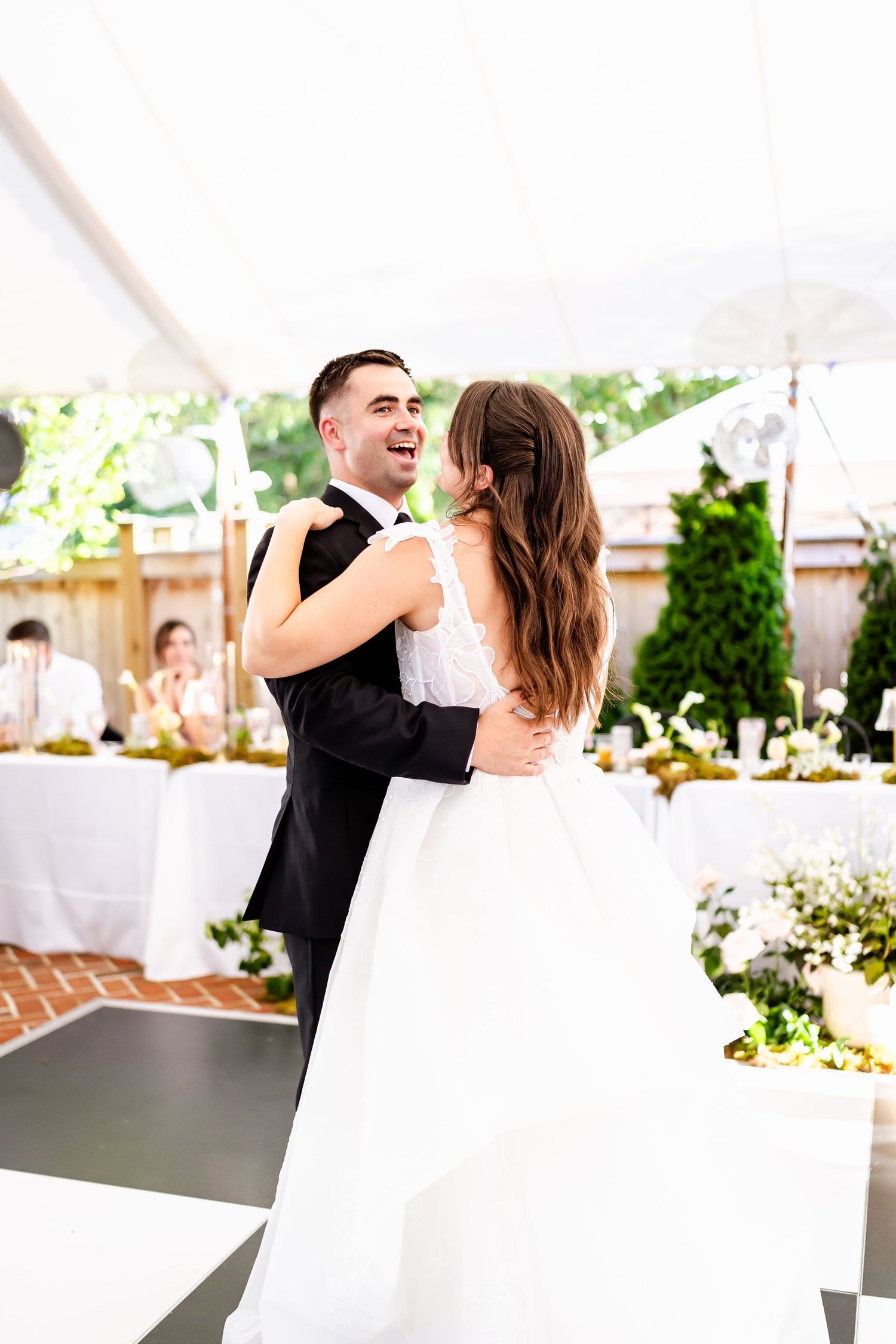 A couple shares their first dance on a black and white checkered dance floor under a white tent.