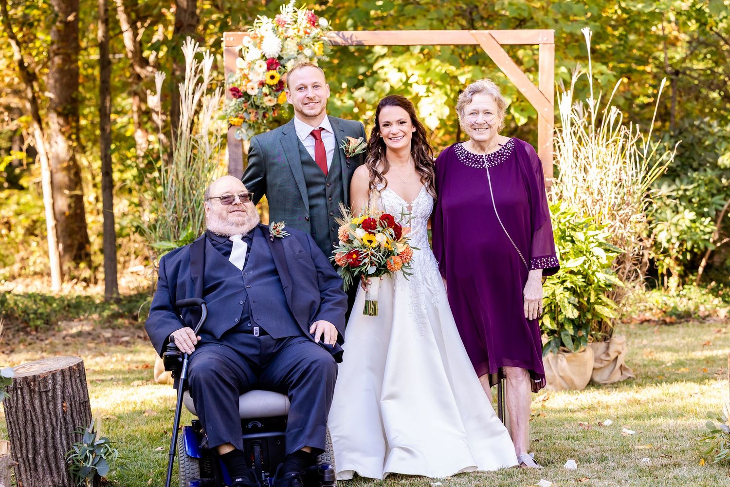 A wedding party poses together outdoors under autumn trees with purple and navy attire.