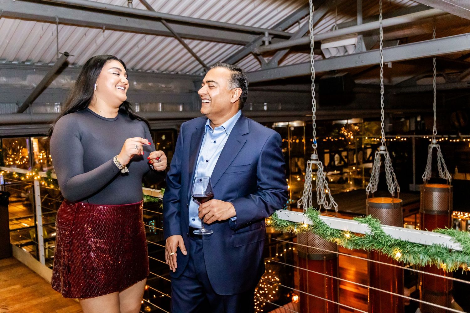 Two people enjoying drinks and conversation at an upscale bar with pendant lighting and bottles on display.