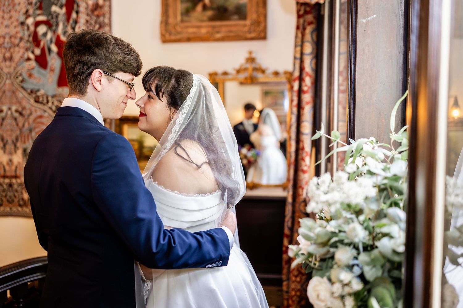 A bride and groom share a tender kiss in an elegant room, with the bride wearing a white gown and veil.