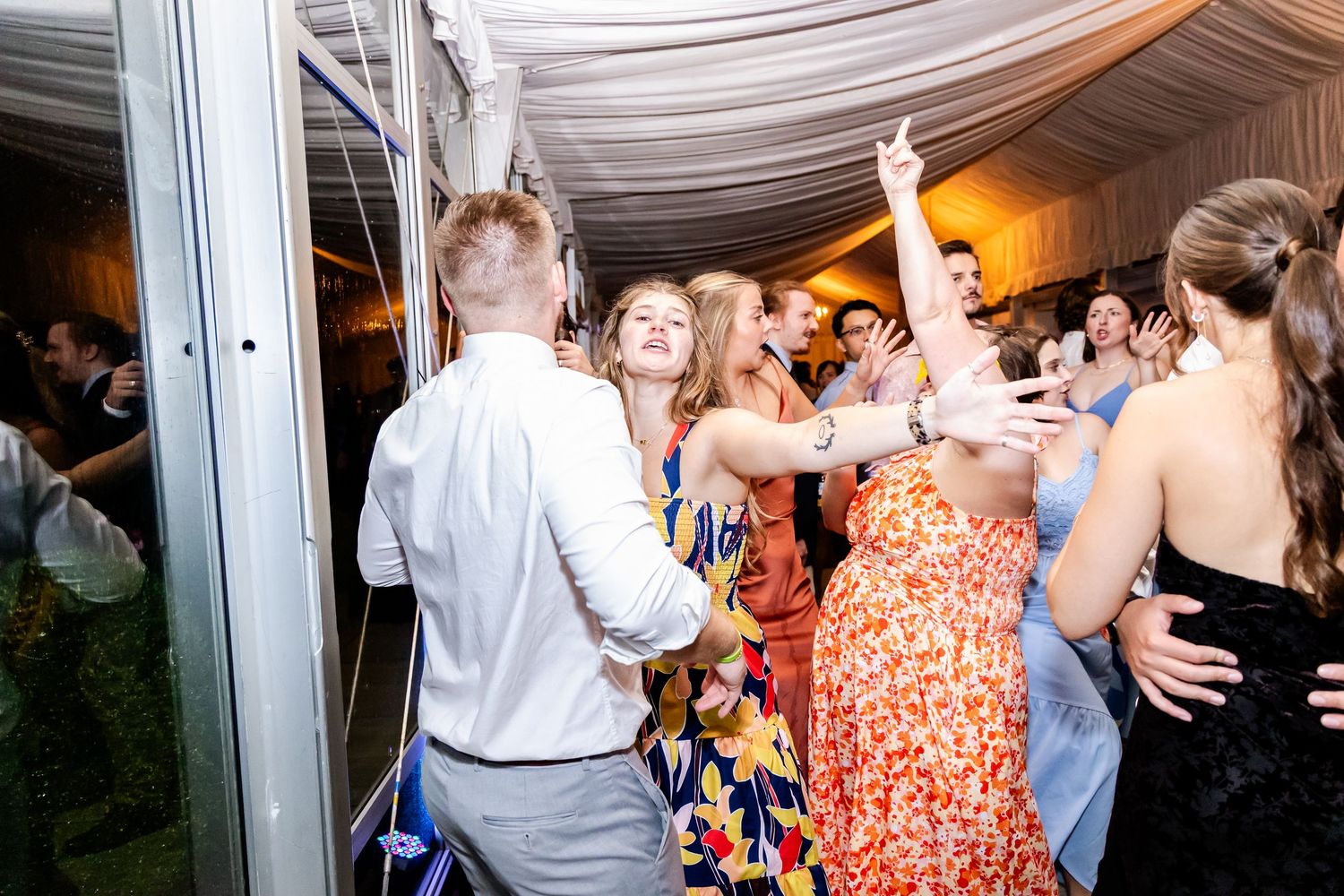 Lively wedding reception with guests dancing under draped fabric ceiling and ambient lighting.