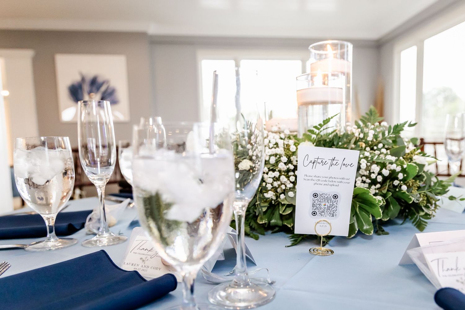 Elegant wedding reception tables with navy and white decor, glassware, and floral arrangements.