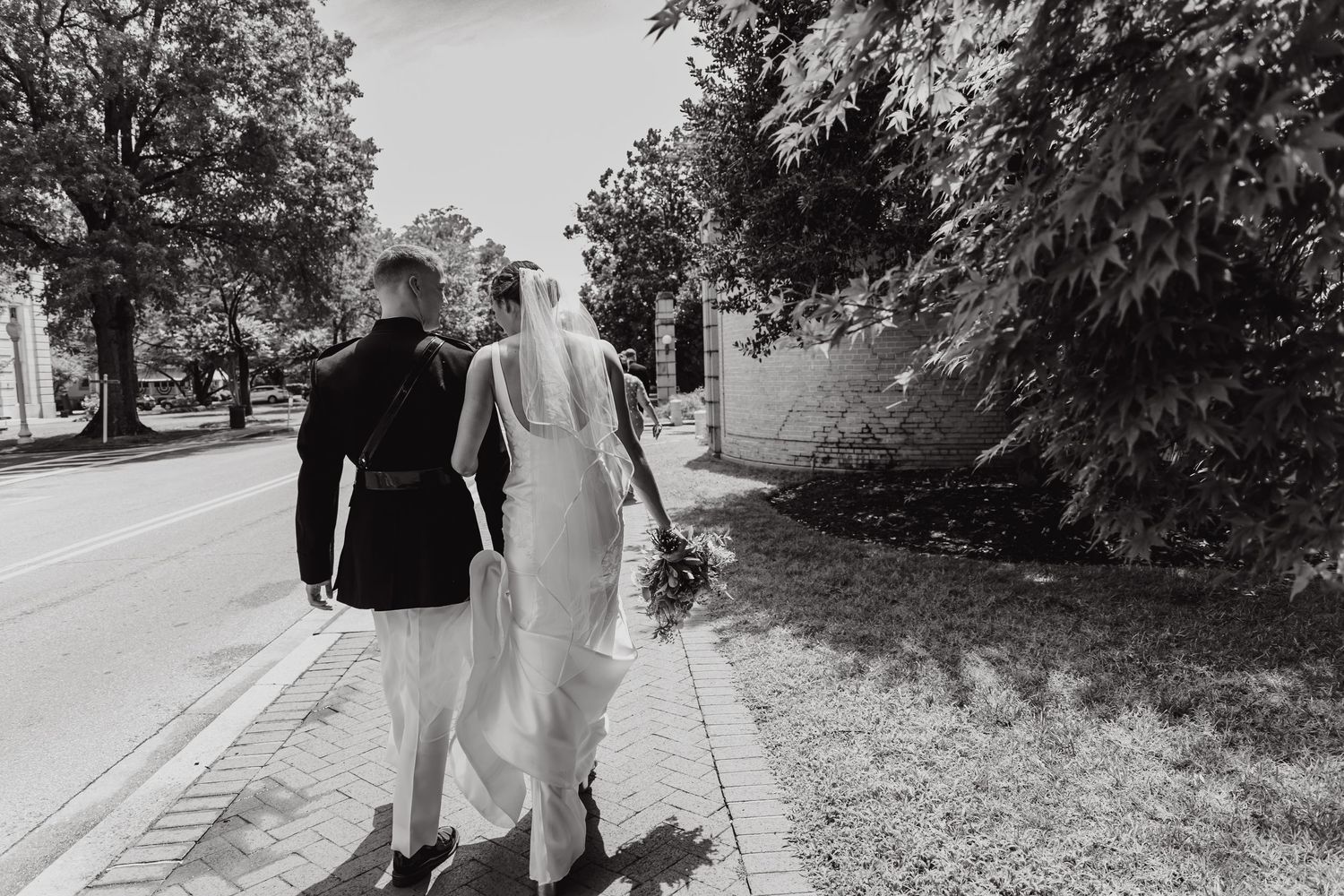 Black and white photo of wedding couple walking along a tree-lined path.