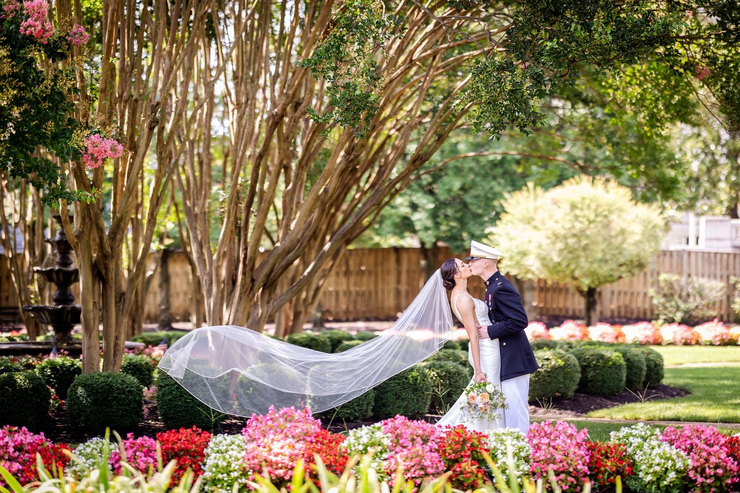 A wedding ceremony setup in a garden with pink azalea flowers blooming and white chairs arranged in rows.