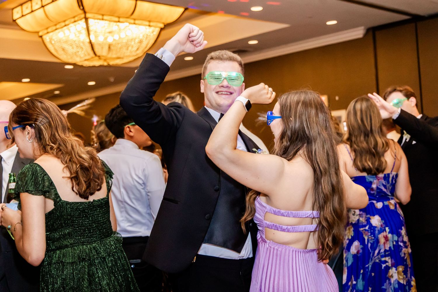 Wedding guests dancing and celebrating with joyful energy under ornate ballroom chandeliers.