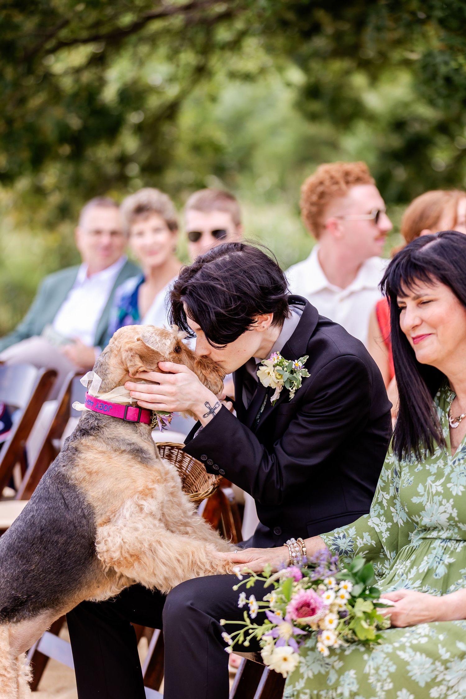 Airedale terrier excitedly jumps up to kiss people during outdoor wedding ceremony.