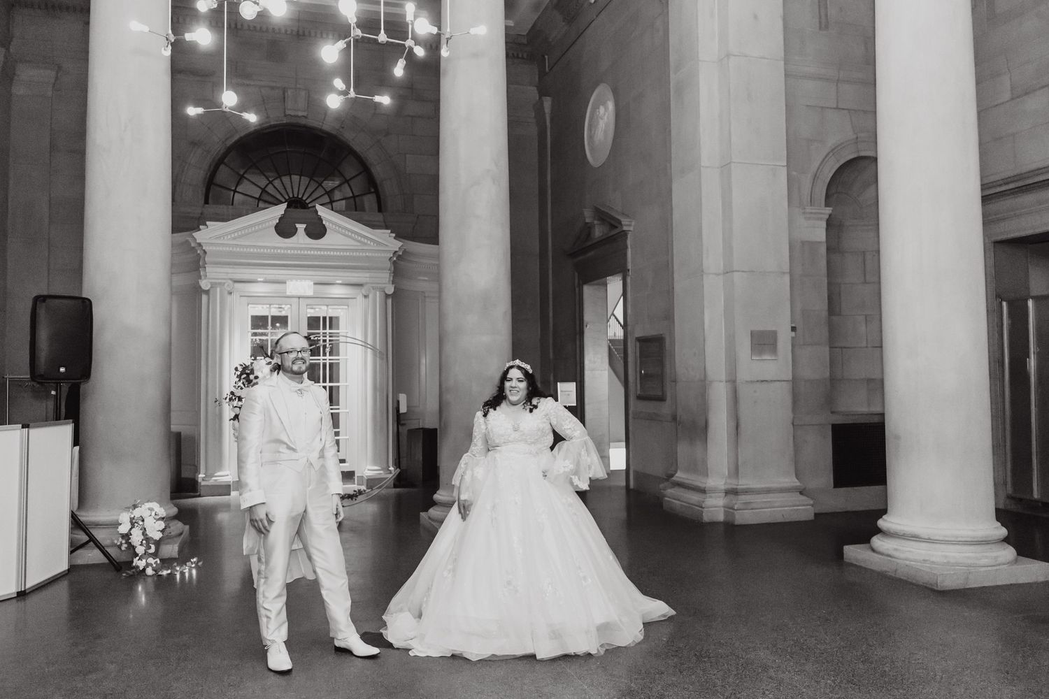 Black and white photo of a couple in a grand historic venue with classical architecture.