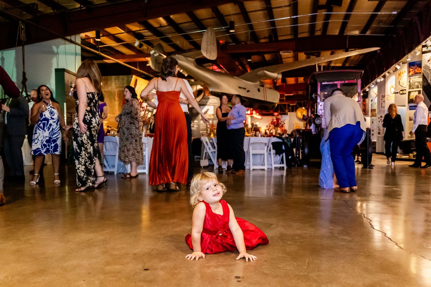 Wedding guests dance at a rustic reception venue with wooden beams and festive lighting.