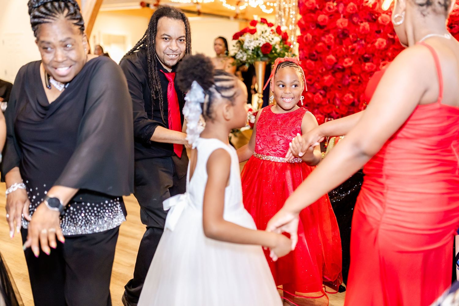 A group dancing together at a party with festive red decorations in the background.