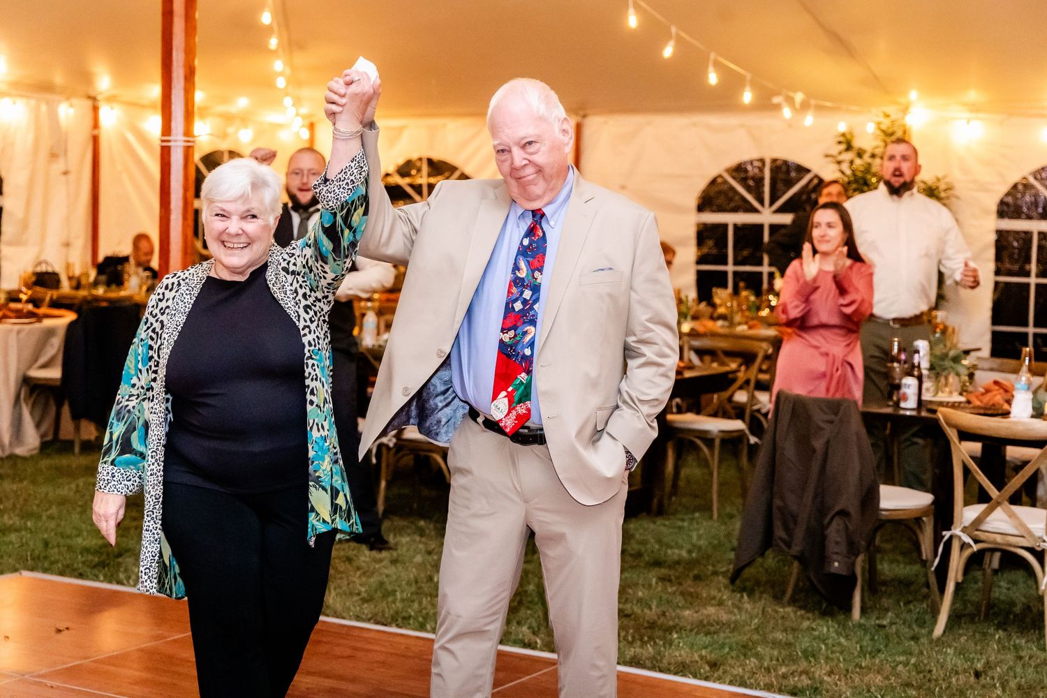 Wedding reception dance party with guests celebrating under string lights in an outdoor tent.