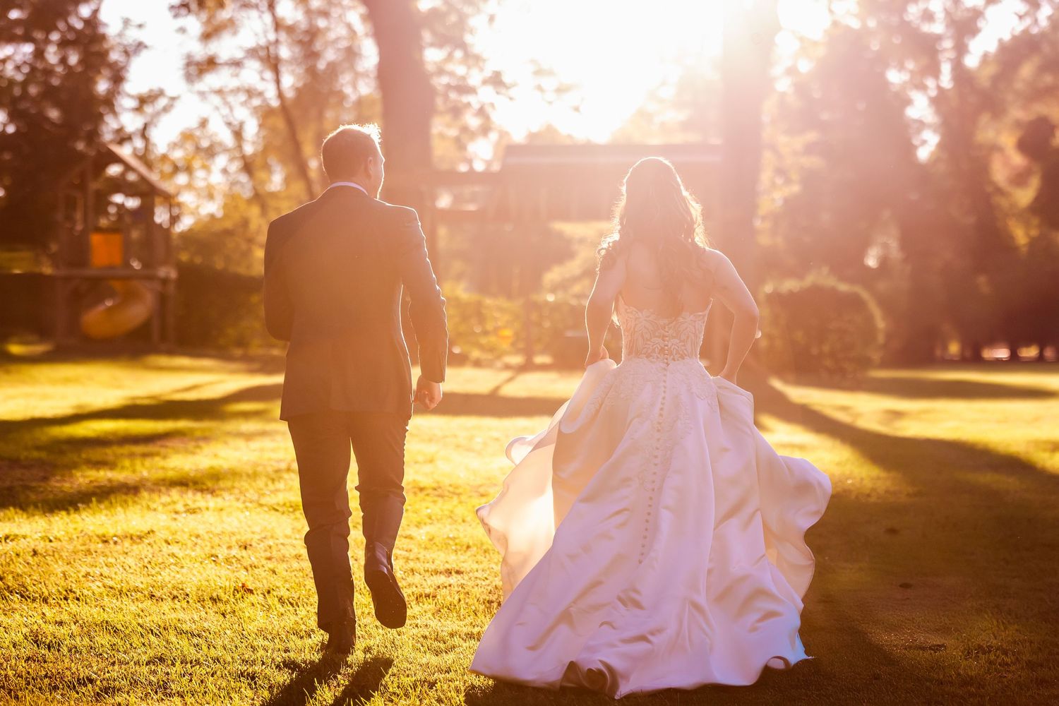 A couple runs together through golden sunlight on their wedding day in an outdoor setting.