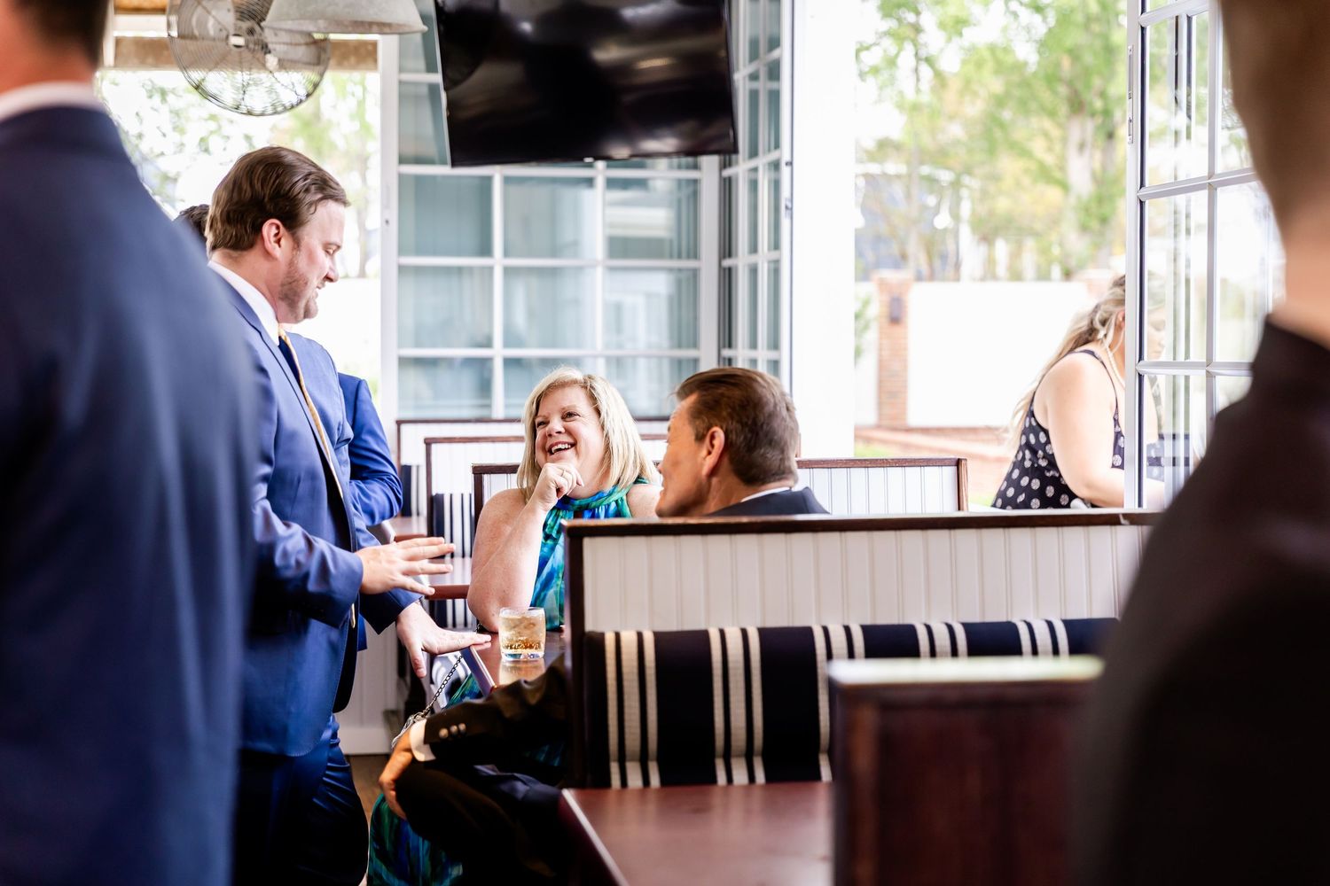 People engaged in conversation at a restaurant bar with natural lighting coming through windows.