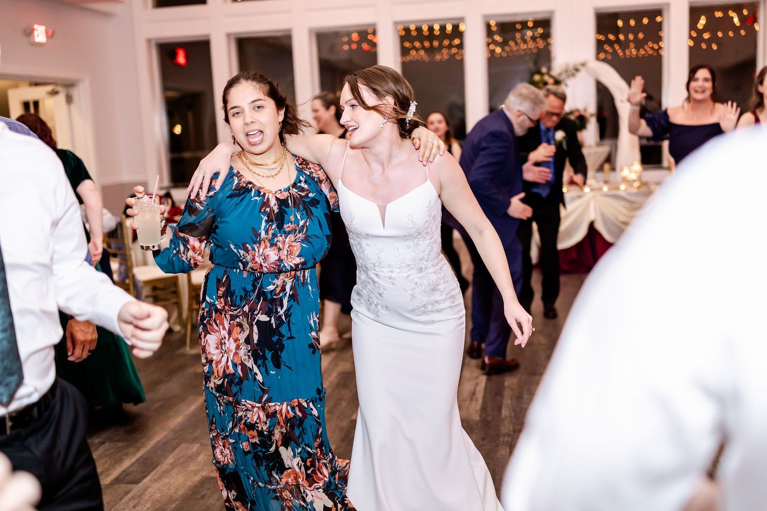 Wedding celebration showing multiple couples dancing in an elegant white-pillared venue with string lights.