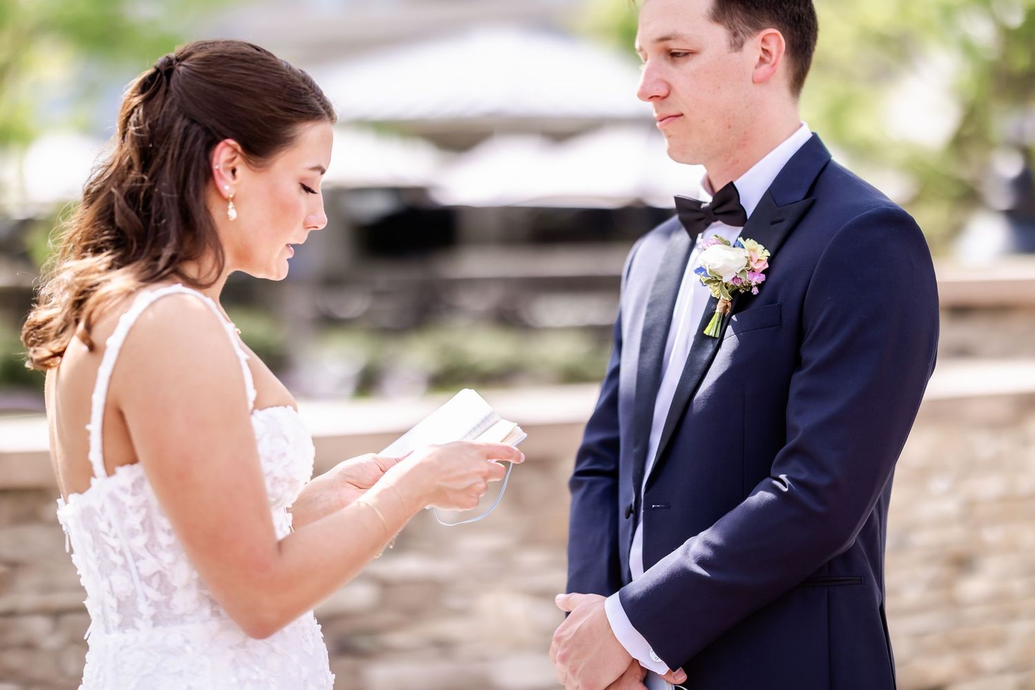 A couple shares a playful moment during their wedding ceremony while exchanging rings outdoors.