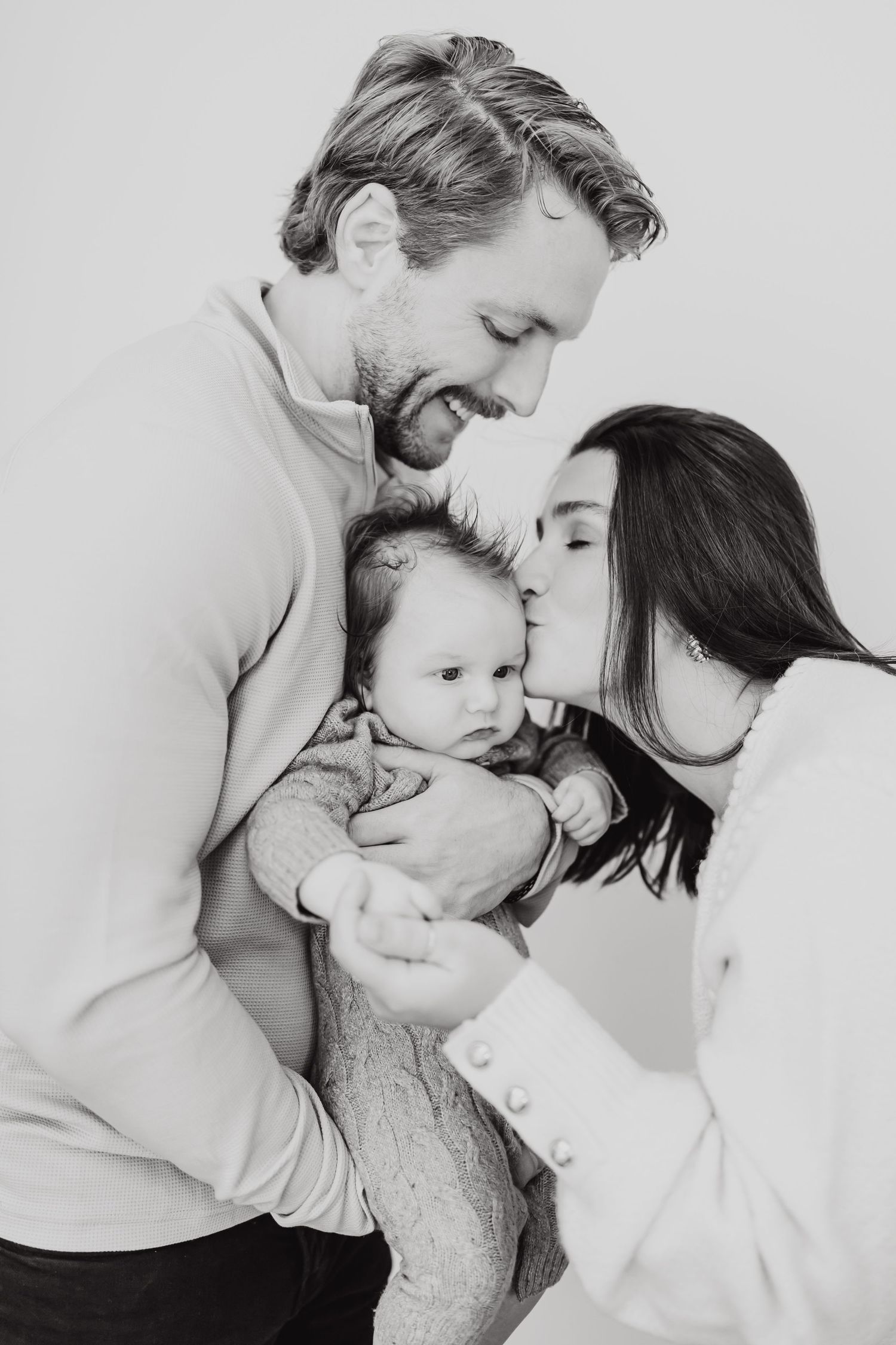 A tender black and white portrait of parents sharing an intimate moment with their baby.