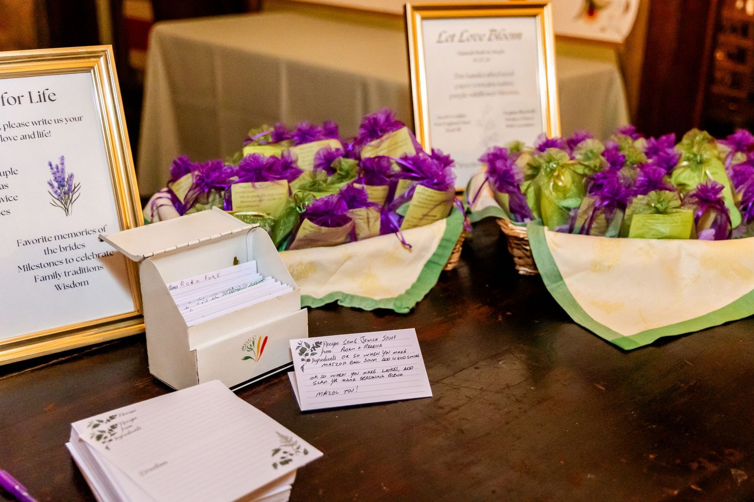 Wedding guest book cards displayed with purple flowers and framed signs on a dark wooden table.