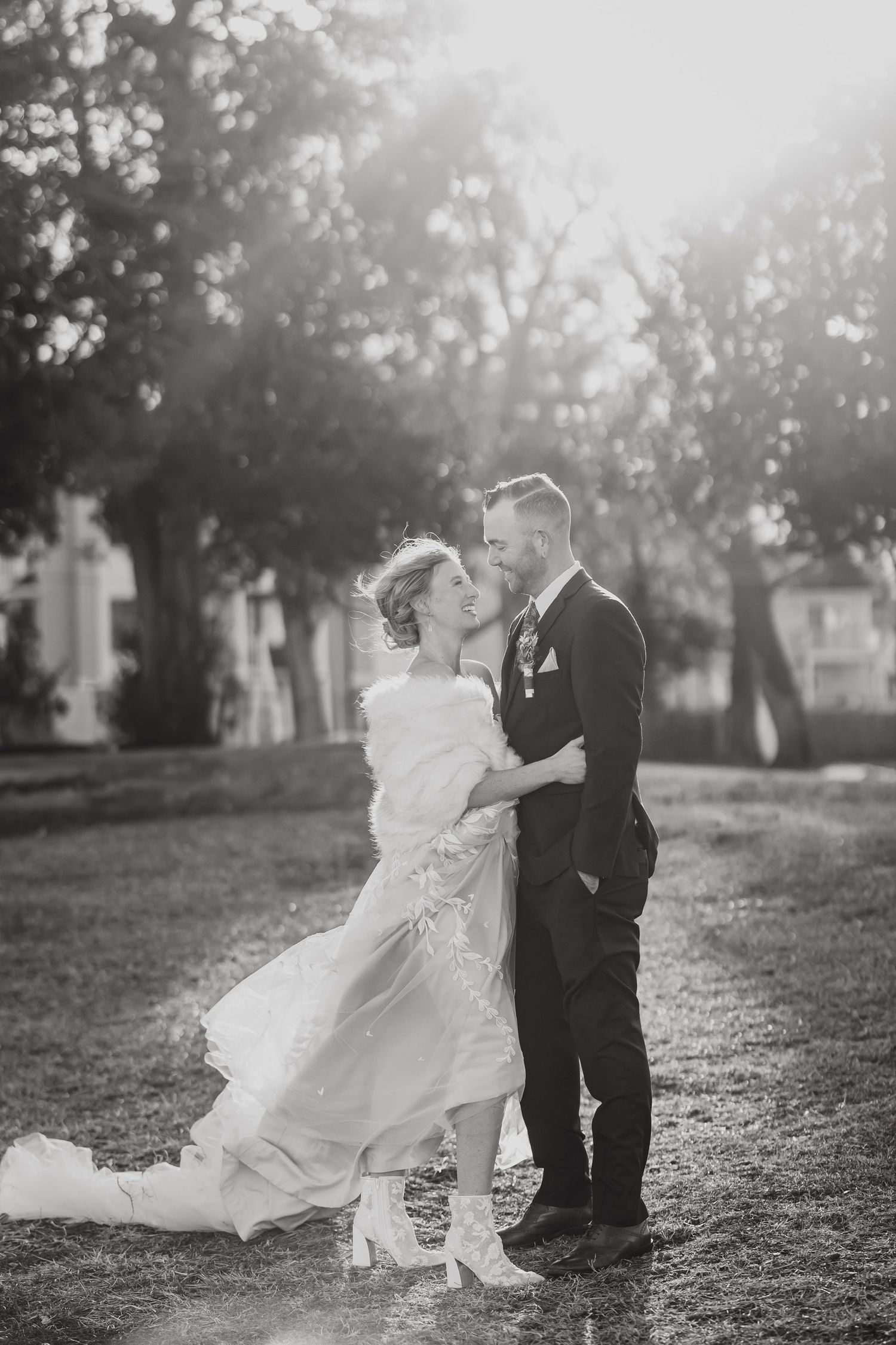 A romantic black and white wedding photo of a couple embracing outdoors with the bride's dress flowing.