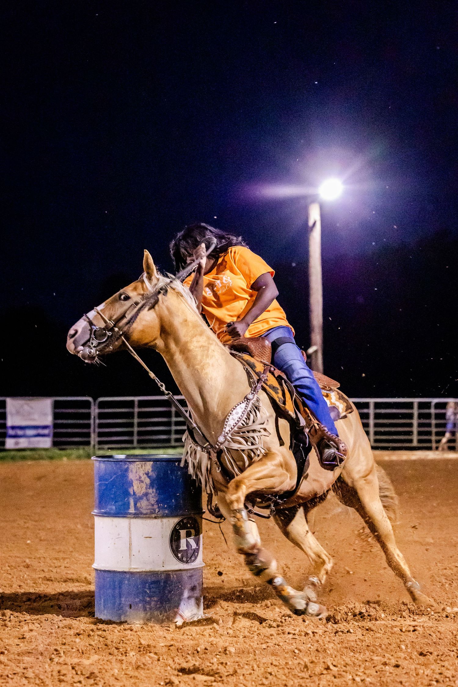 Rodeo rider navigates a barrel racing course on a palomino horse under bright arena lights at night.