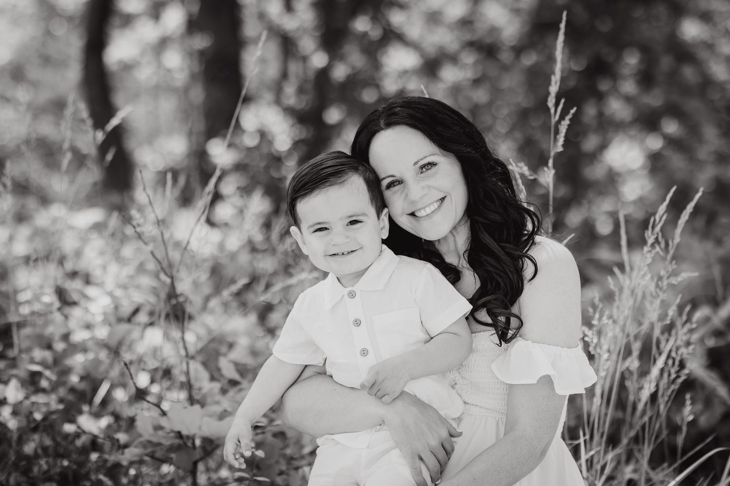 Black and white photo of mother and baby sitting amongst wildflowers in a natural outdoor setting.