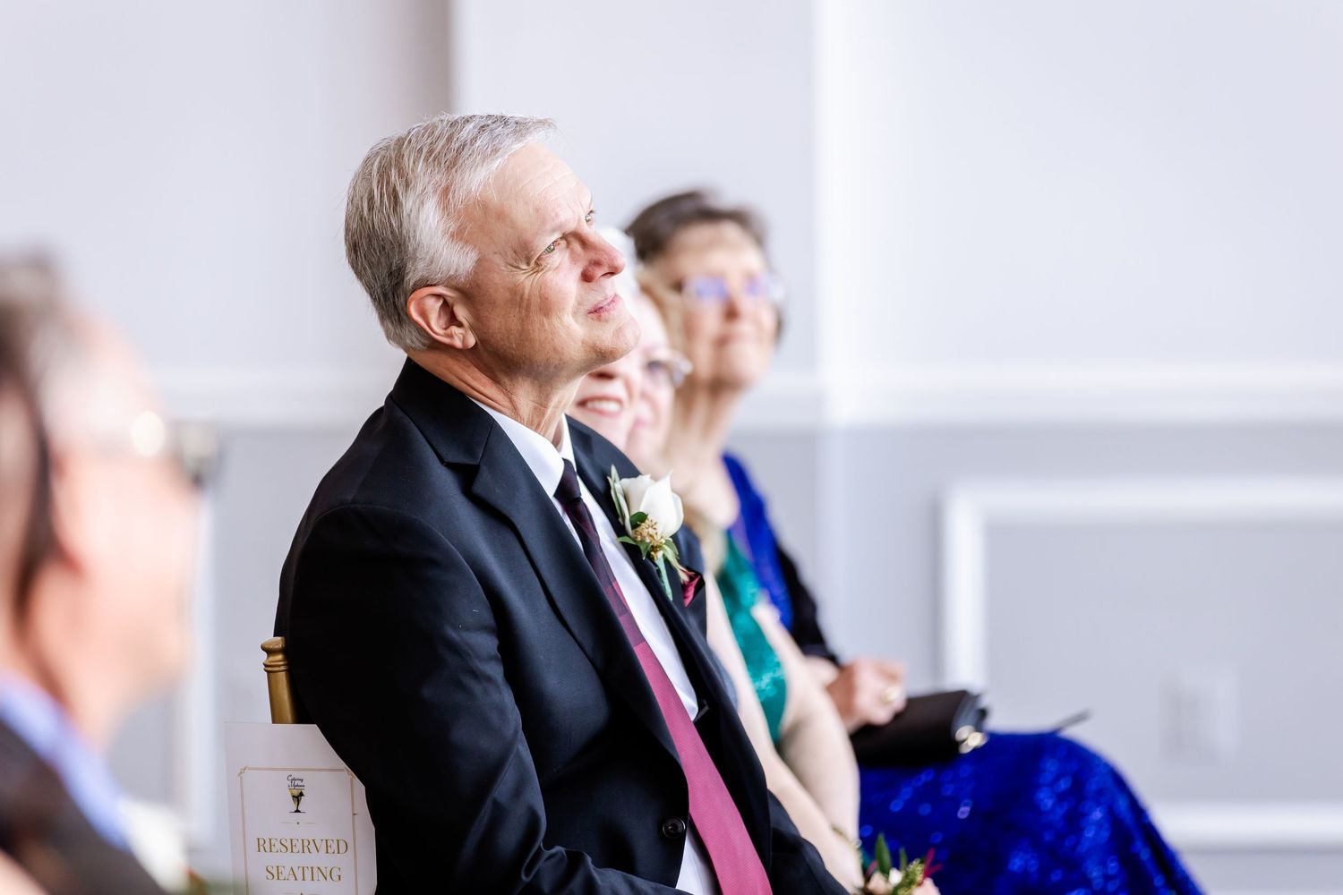Wedding guests sit in formal attire during an indoor ceremony.