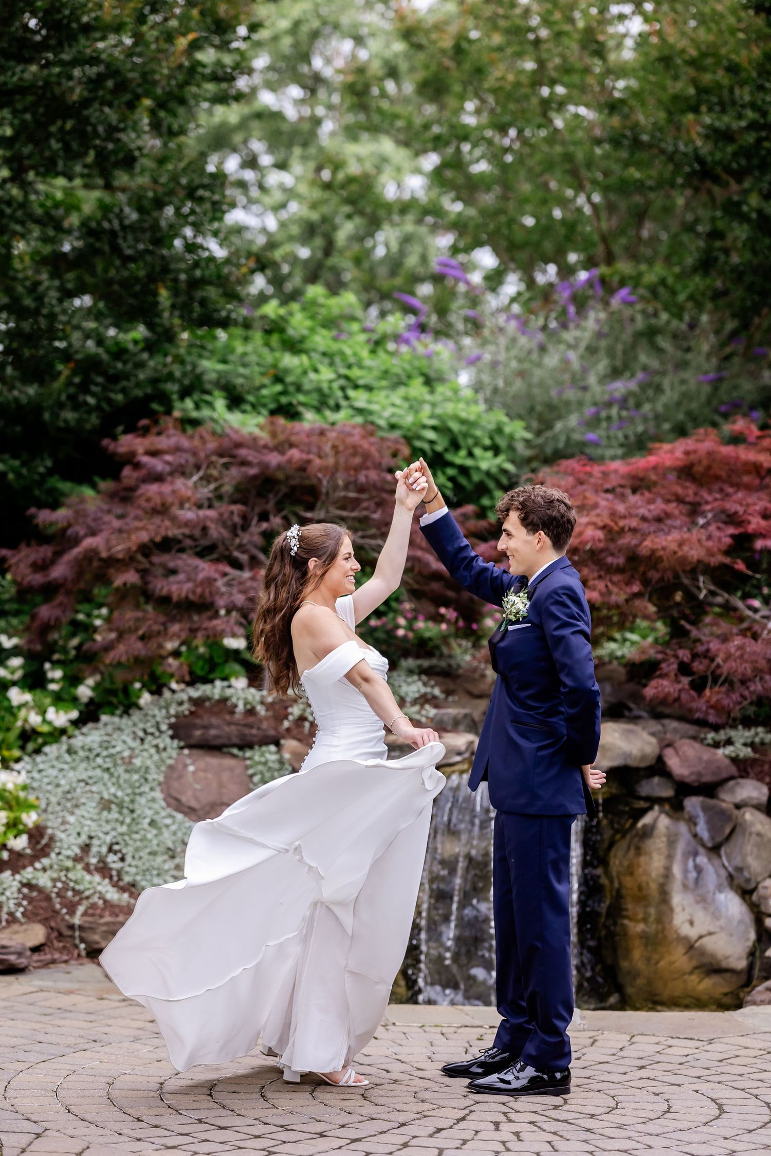 A couple dancing together on a stone patio surrounded by vibrant red Japanese maple trees and lush gardens.