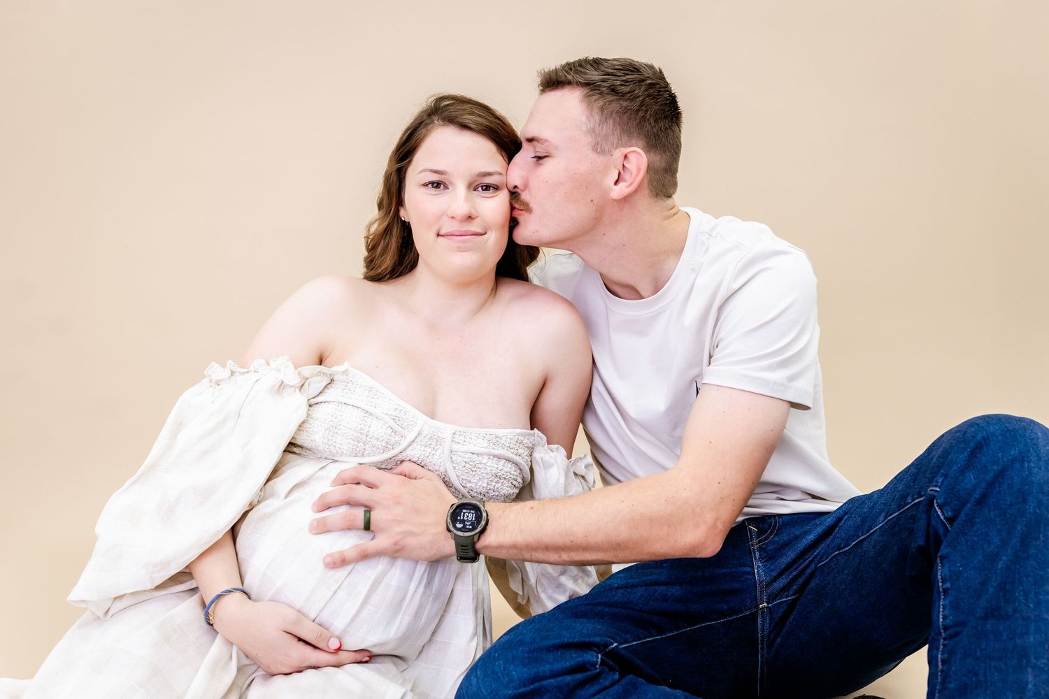 A couple sitting close together, with the person on the right kissing the other's cheek affectionately.