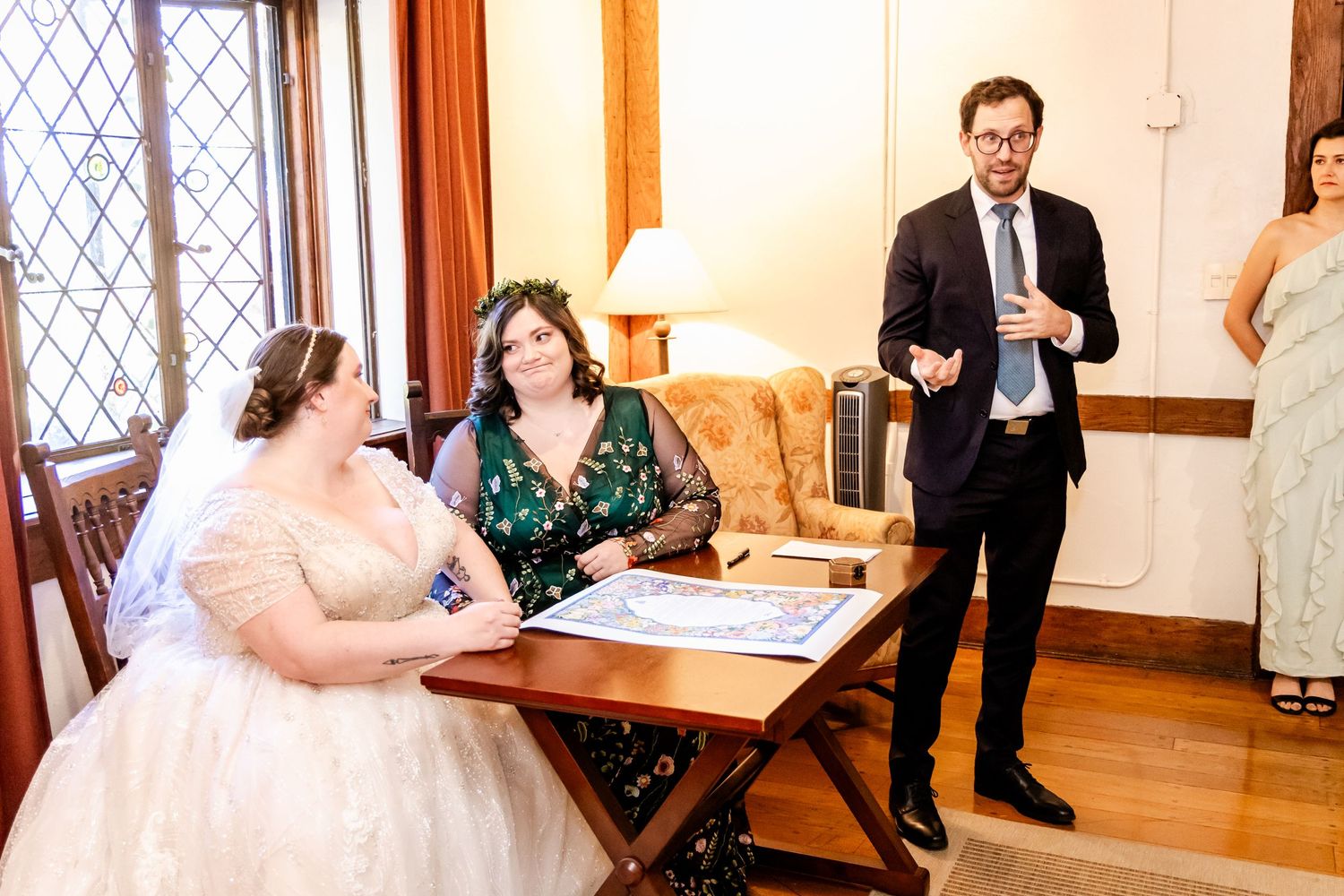 Wedding scene showing people gathered around a table signing documents in an elegant room.