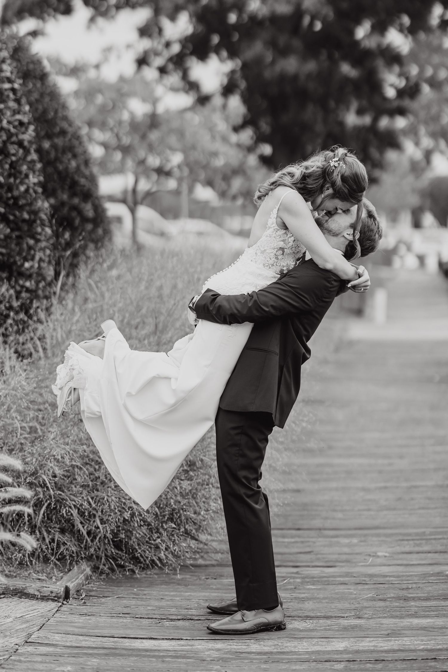 Black and white series showing romantic dip poses on wooden boardwalk during wedding photoshoot.