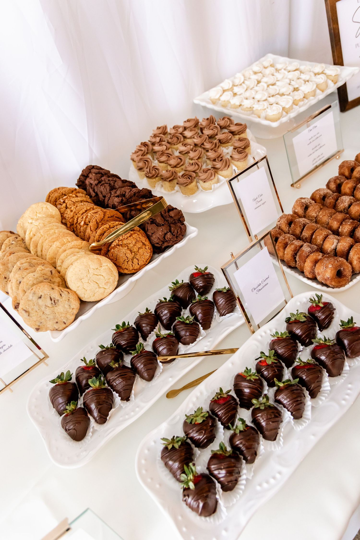 Elegant dessert display featuring chocolate covered strawberries, cookies and various sweet treats.