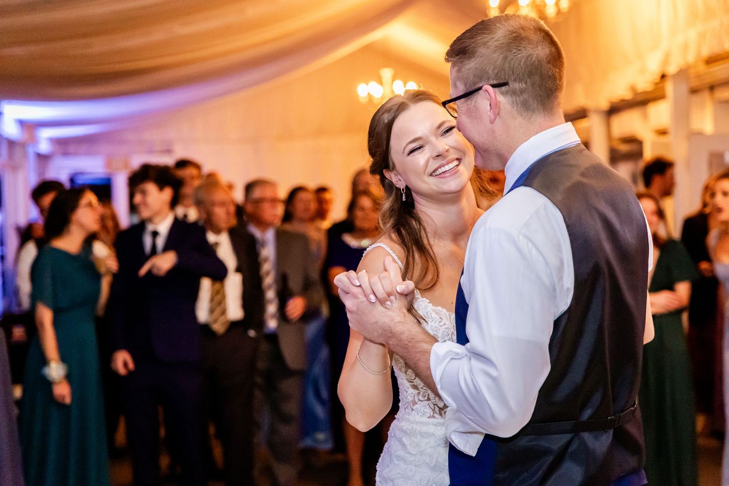 Couple shares a joyful dance moment at their wedding reception with guests looking on.
