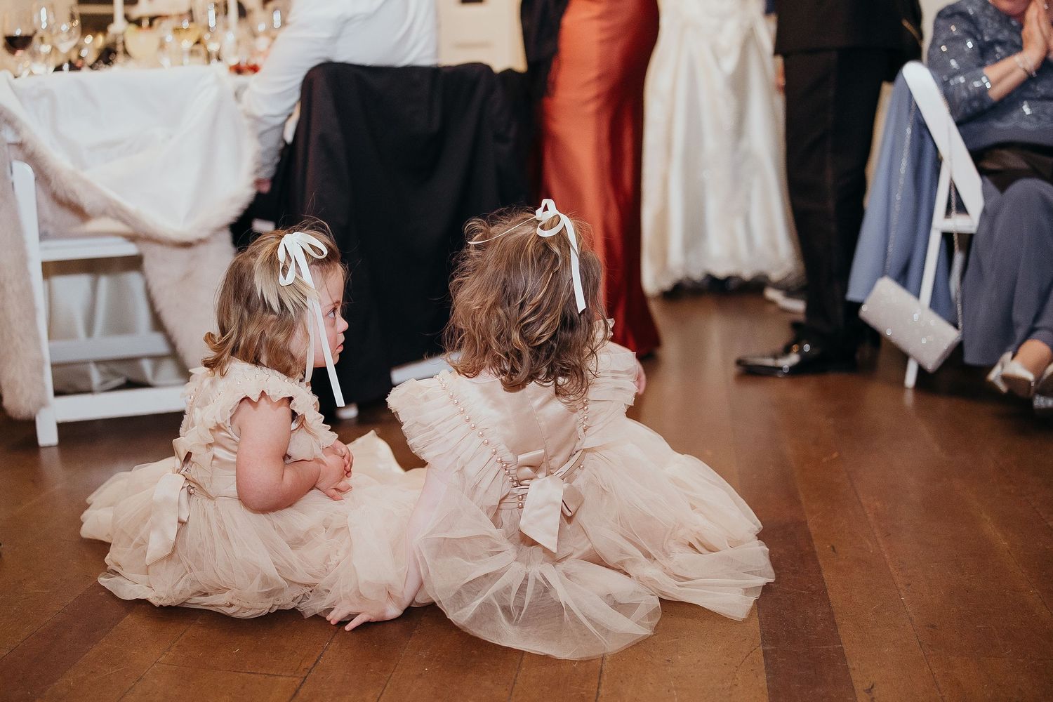 Two flower girls in pink tulle dresses sitting on a dance floor at a wedding reception.