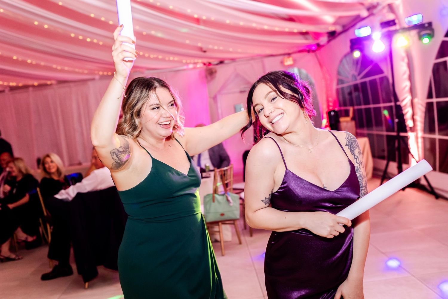 Two guests dancing and enjoying themselves under pink lighting at a wedding reception.