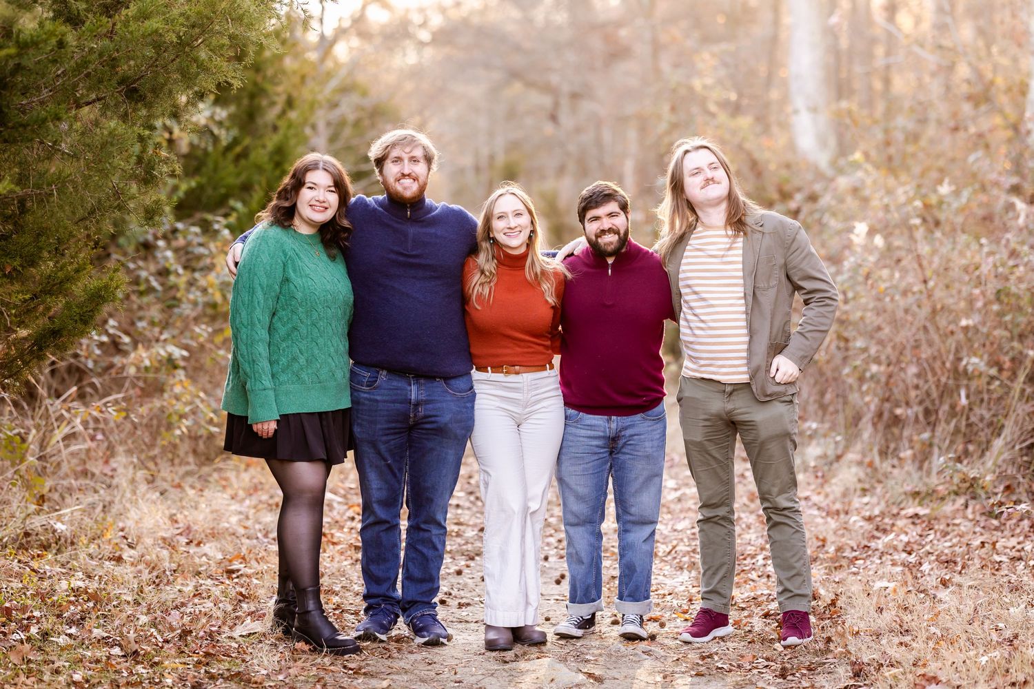 A group portrait of five people standing together on a fall trail wearing colorful sweaters.