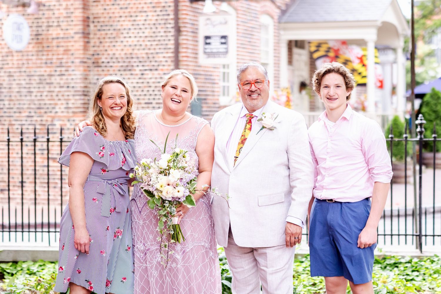 Wedding party members in pastel dresses pose outside historic venue.
