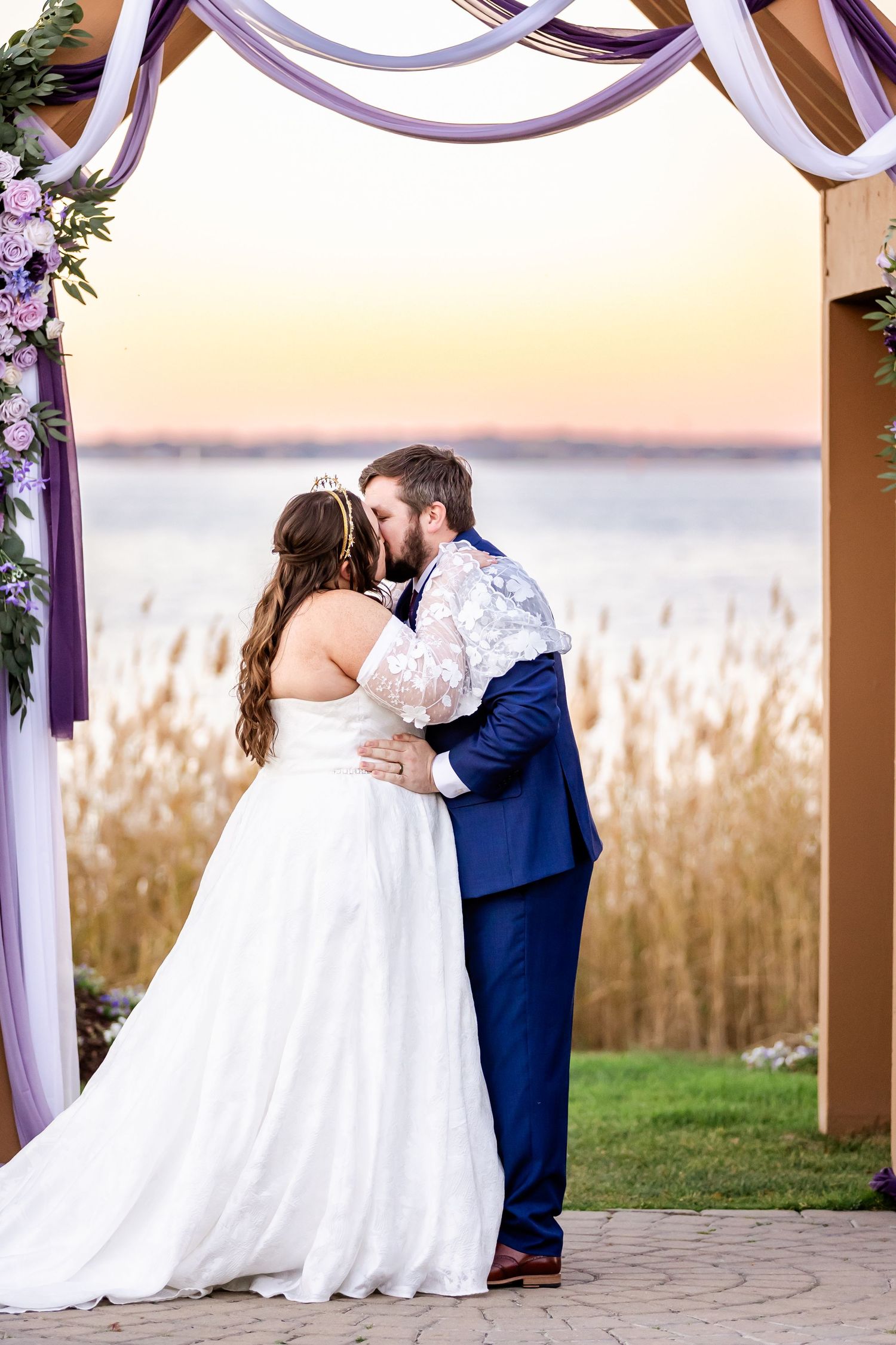 Newlyweds share an intimate moment under a decorated wedding arch at sunset.
