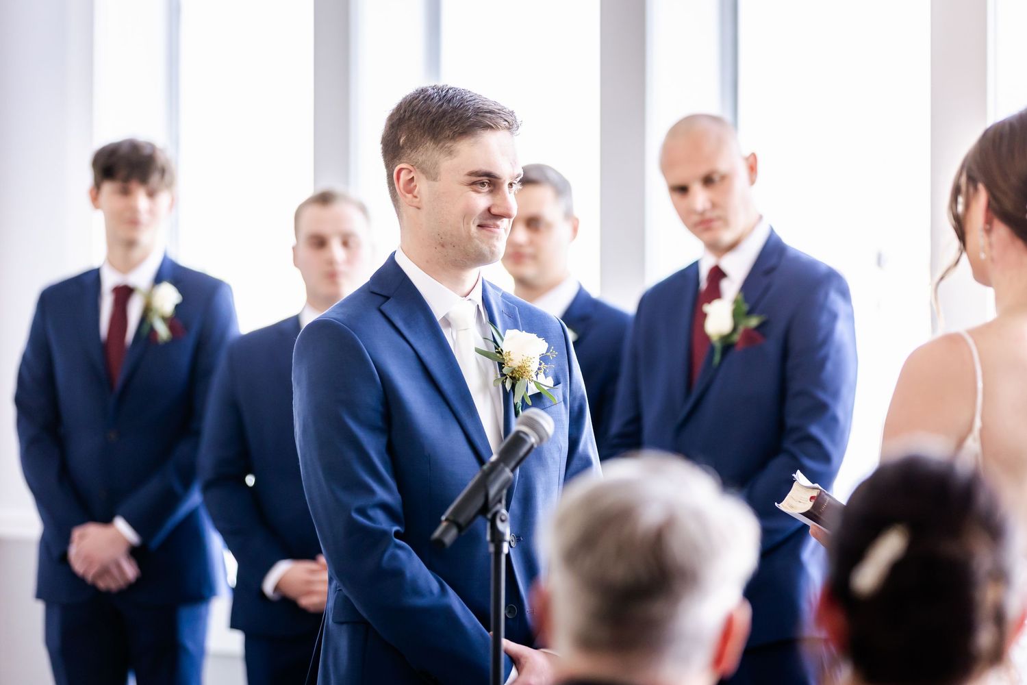 A groom in a navy suit delivers wedding vows at the altar while groomsmen stand behind him.