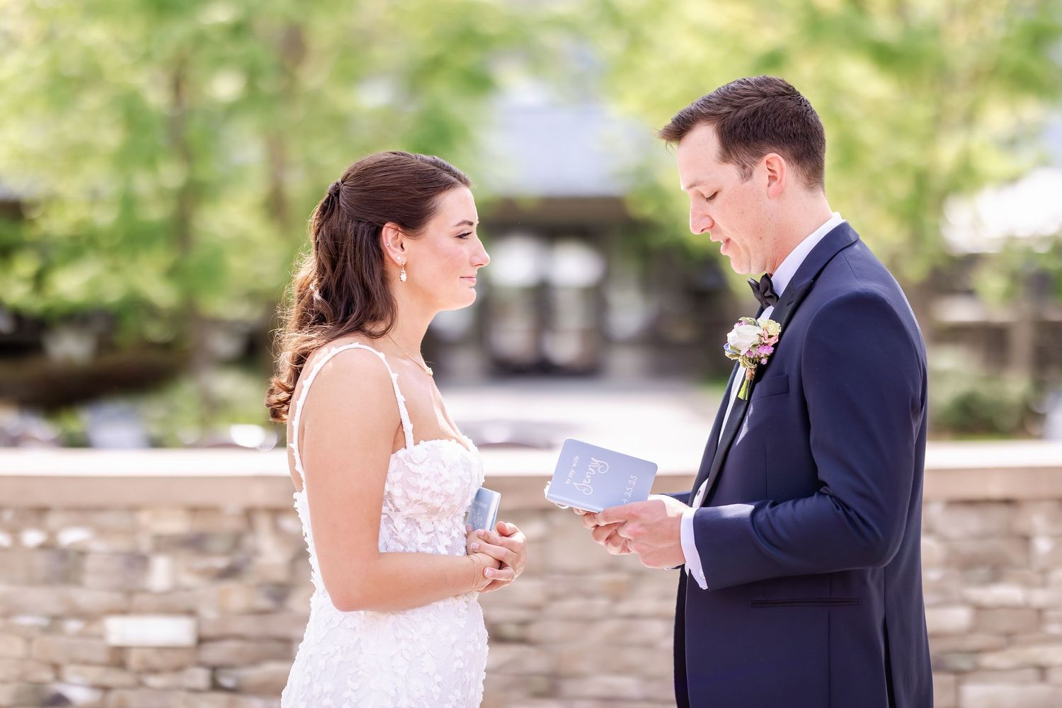 A couple shares a romantic moment during their outdoor wedding ceremony against a stone wall backdrop.