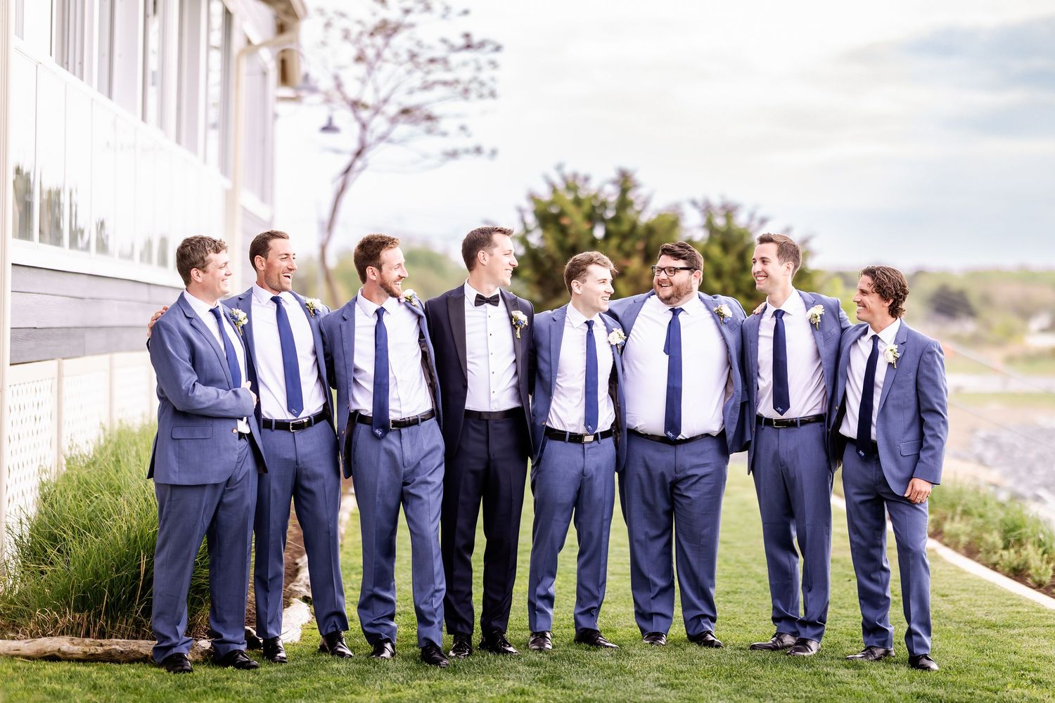 Groomsmen in matching navy blue suits pose in a line against a stone wall backdrop.