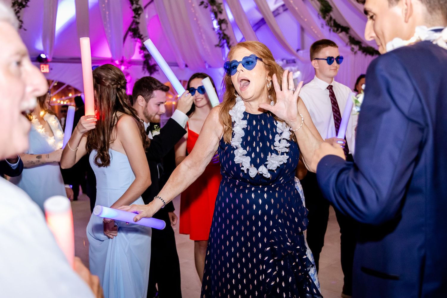 Wedding reception dance floor illuminated with purple lighting and guests dancing.
