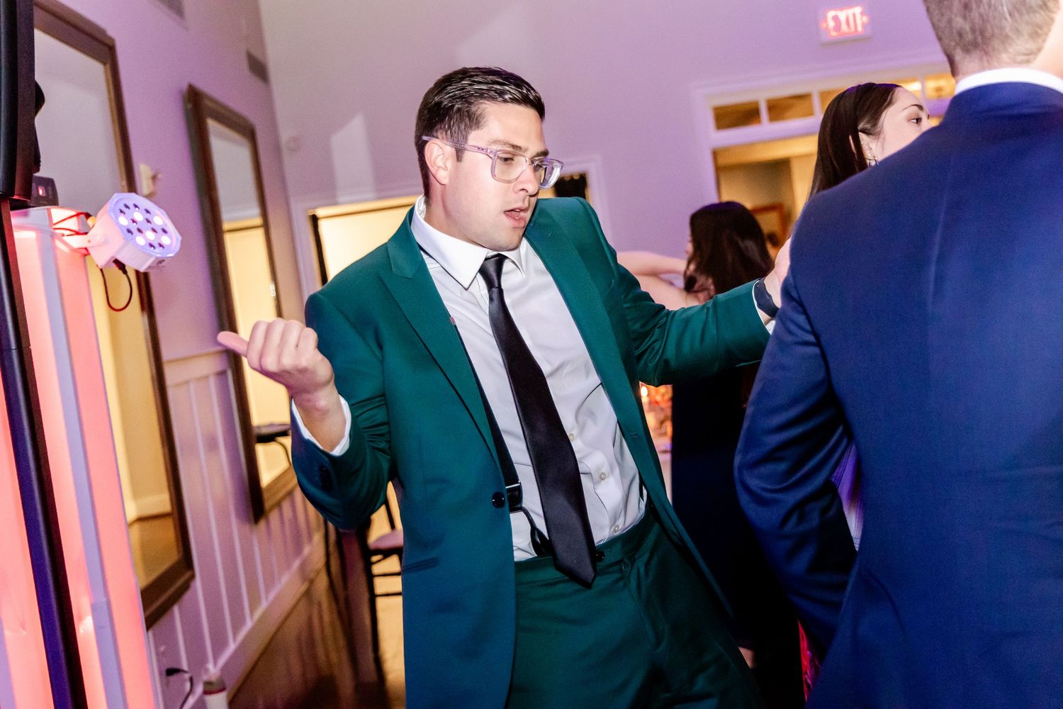A guest in a green suit jacket dances enthusiastically at a wedding reception.