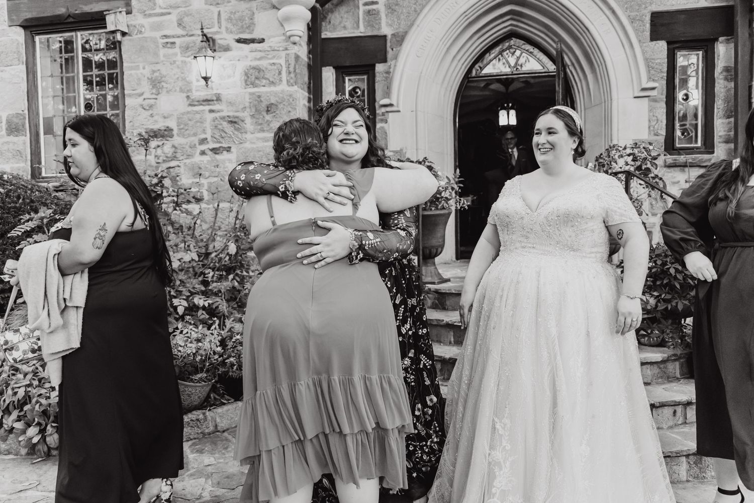 Wedding party in black and white dresses posing outdoors in front of stone building.