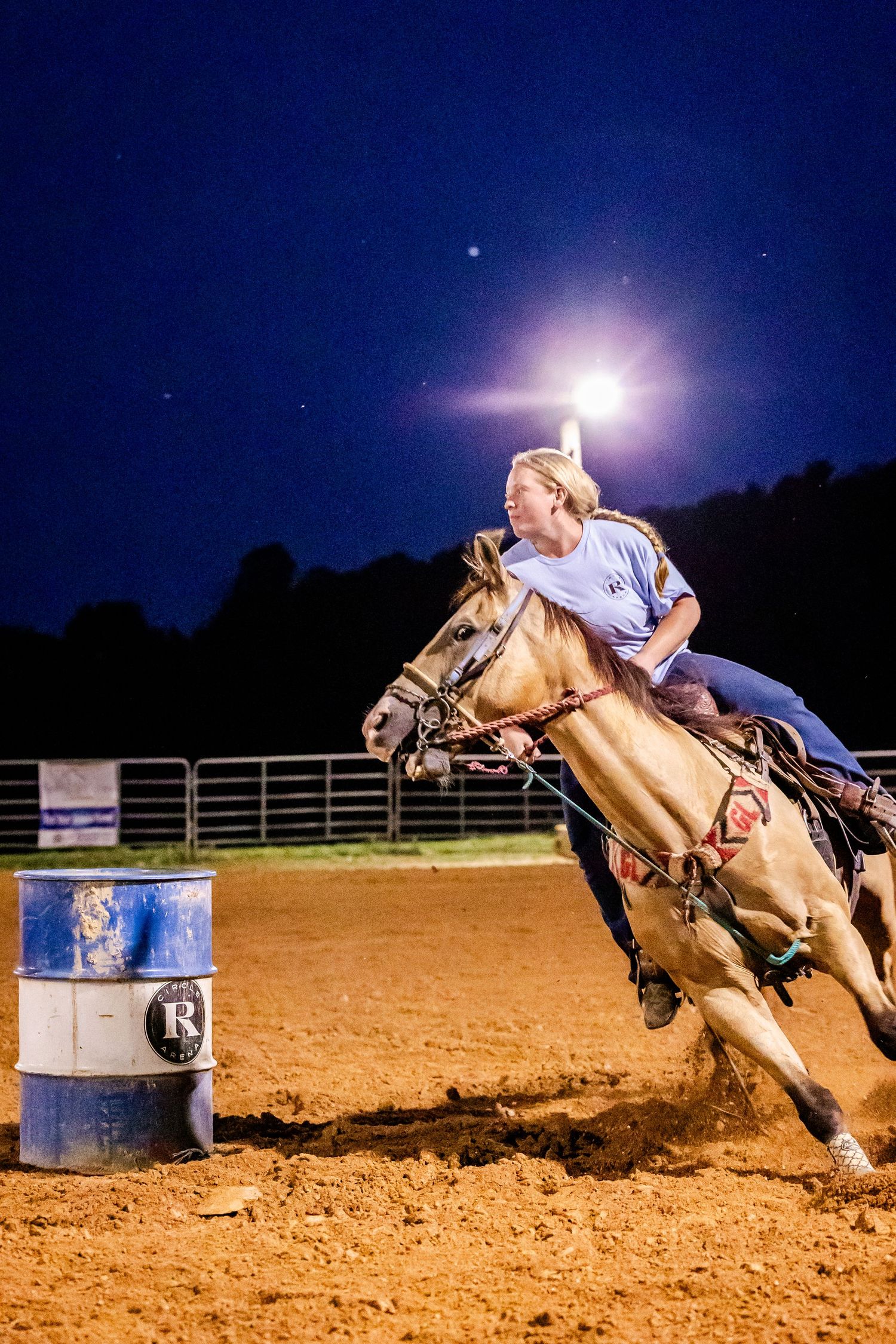 Horse and rider navigating around a barrel under bright arena lights at night.