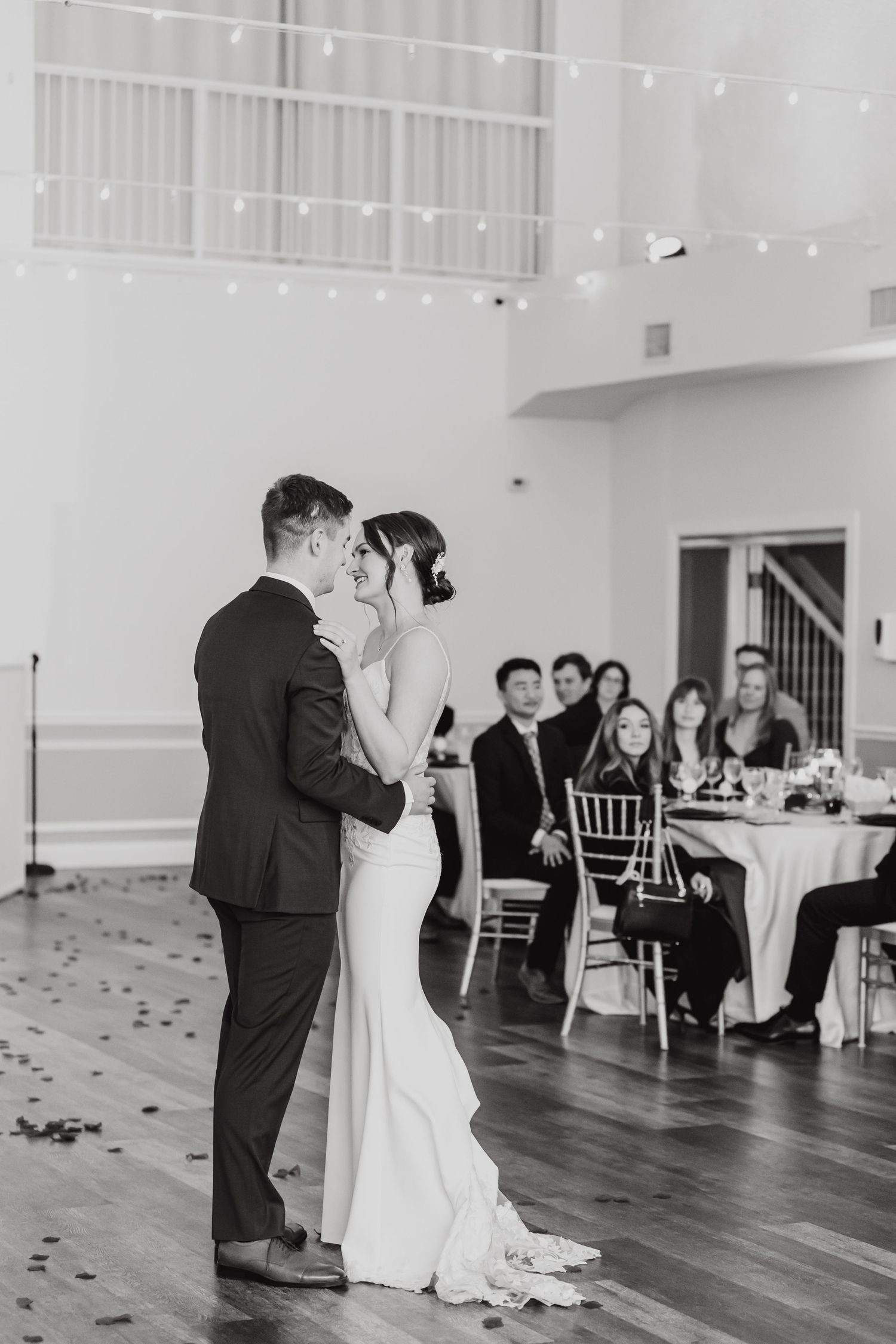 Couple shares their first dance in an elegant white reception hall with hardwood floors.