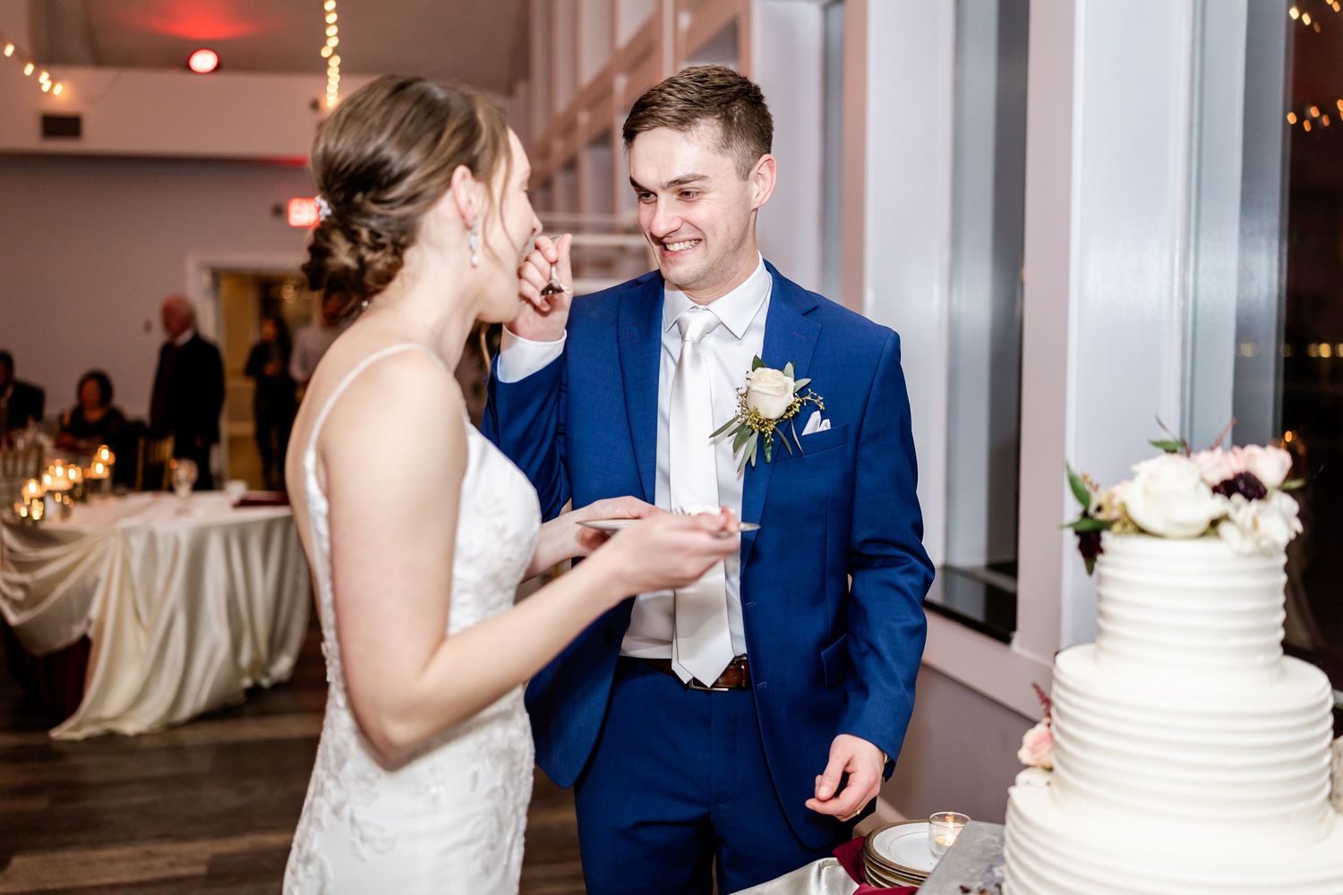Couple shares their first bite of wedding cake at an indoor reception venue.