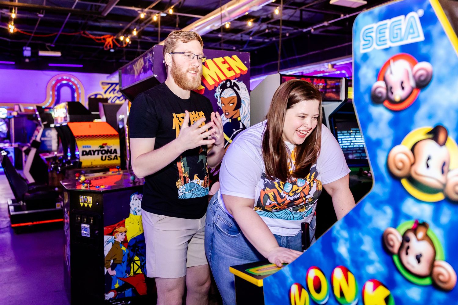 Gamers enjoying arcade games in a neon-lit retro arcade with colorful Monkey Ball cabinet visible.