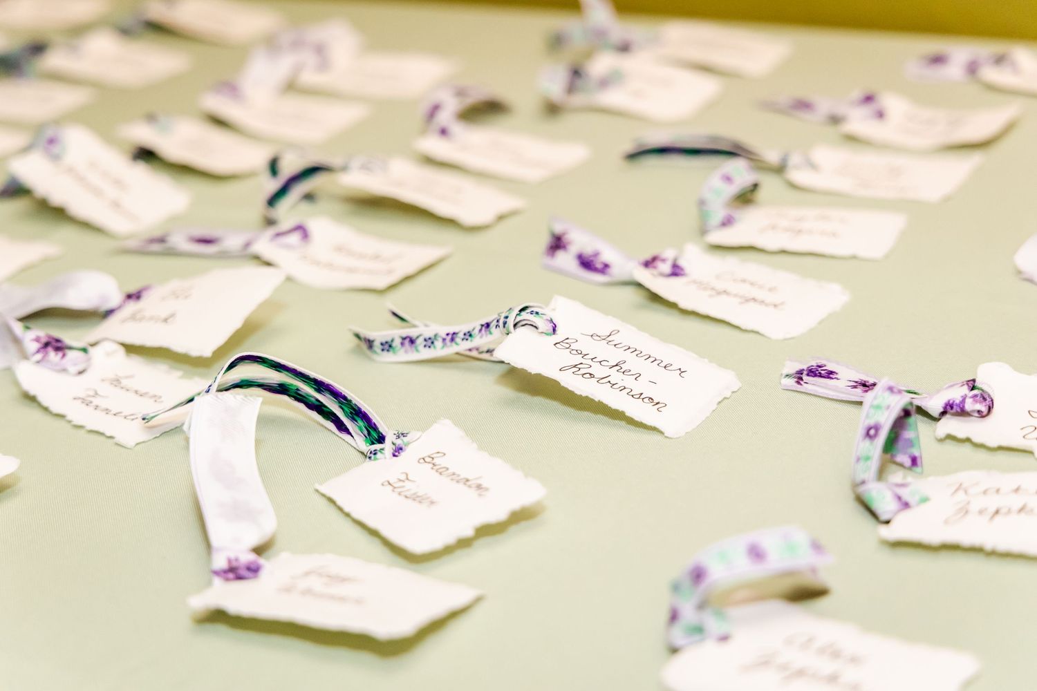 Wedding place cards with purple ribbons arranged on light green surface.