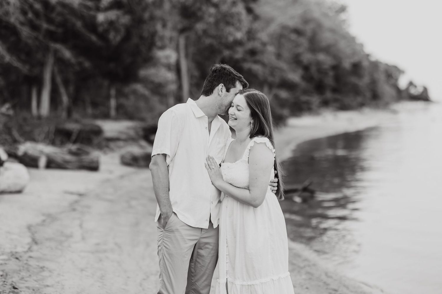 A couple stands close together in an intimate moment on a beach shore in black and white photography.