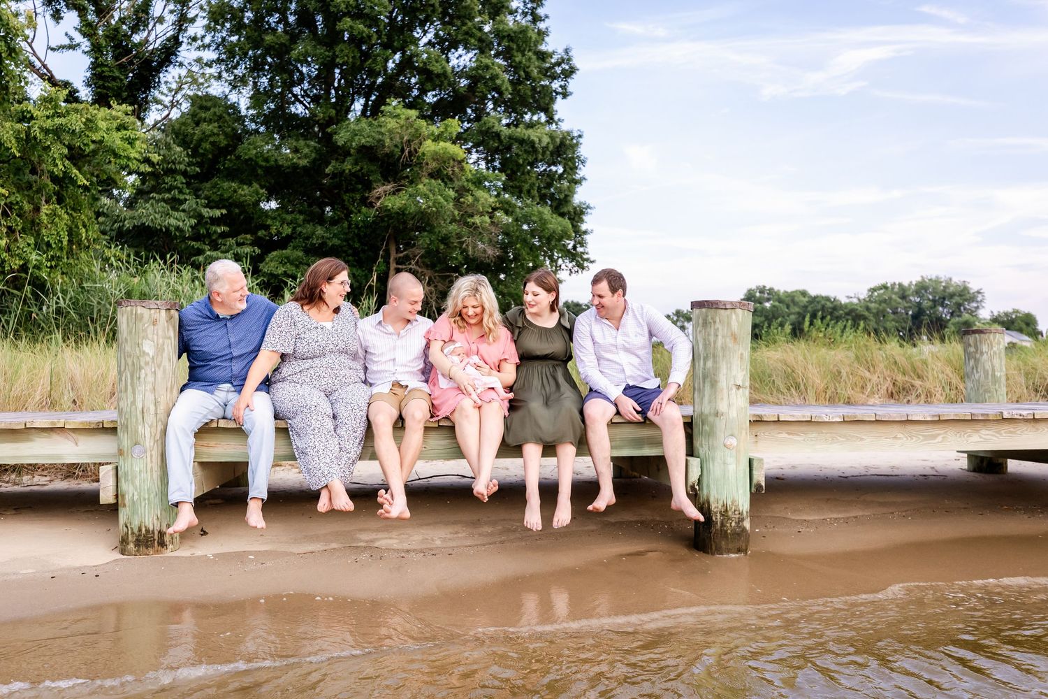 Group of people sitting and laughing together on wooden dock by the water.