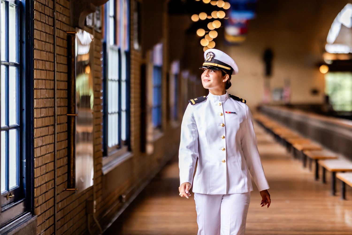 Naval officers in white uniforms walking through a brick hallway with ambient lighting.